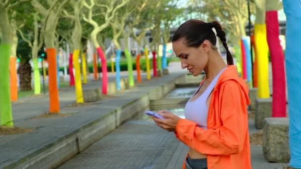 Smiling sports girl standing on the street and typing a message to her boyfriend — Stock Video
