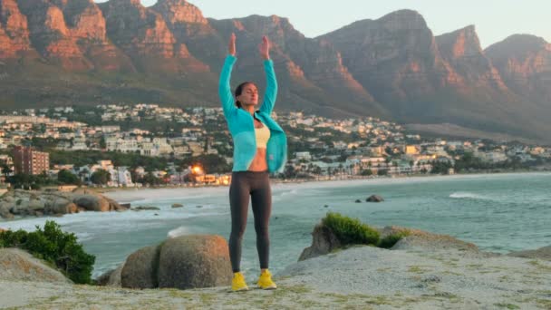 女徒步旅行者在山顶张开双臂 年轻健康的女人在山顶悬崖边练习瑜伽 穿紧身裤的女运动员在海滩上参加体育运动 山岭背景下的女孩 — 图库视频影像