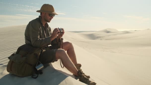 Man Travel Clothes Sits Sand Dune Desert Takes Photo Film — Vídeo de Stock