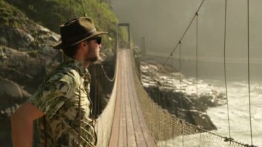 Tatil konseptinde mutlu gezginler. Komik gezgin yolculuğunun tadını çıkar ve maceraya hazır ol. Norveç 'in İskandinav manzarası üzerinde tahta bir köprüden geçen kayalık yolda bir turist yürüyüşçüsü..