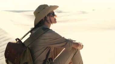 hikers climb up to the sand dune in the red desert. girl in a hat and safari style sits on the sand among the desert. girl lost in the desert in africa. millennial tourist walks out across a sand dune