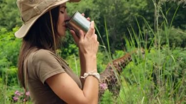 Sırt çantalı güzel bir gezgin dağda dikilirken su içiyor. Kum çölü safarisinde su içen bir kız. Bir kadın zoolog turist demir bardağından su içiyor ve bir zürafayı izliyor.