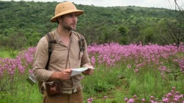 a man tourist in travel overalls and a safari hat stands near the Amazon and looks at the route on the map. a traveler in the savannah in africa explores routes among the jungle in the national park