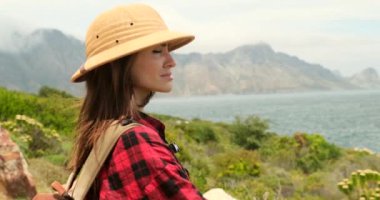 woman traveler with backpack holding hat and looking at amazing mountains and Sea, wanderlust travel concept Tourism, travel, vacation on the rocky sea. a girl in safari clothes stands on the peak