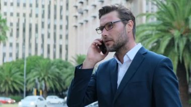 business man uses a tablet and speaks by phone . Student using tablet and speaks by phone in the outdoor. male holding a phone with case. a man in a suit speaks on the phone in new york on wall street
