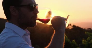 wine bottle and glass on wodden barrel. on a wooden table there is a bottle of wine and a glass of red wine at sunset, a man shows a heart of hands. sommelier waiting for his new vintage of grapes