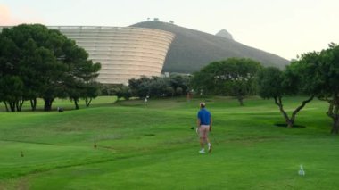 Golfer Hitting Ball with Club on Beatuiful Golf Course. Smiling african american man in cap and sunglasses playing golf. cape town, south africa, stadium, Golfer with golf club taking a shot