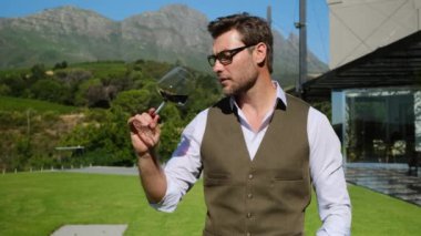 Man toasting wineglasses in a luxury restaurant. stylish successful man in a white shirt in a restaurant drinks wine against the backdrop of mountains. male sommelier testing a new variety of wine
