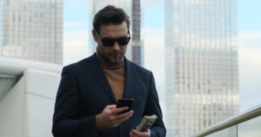 Middle aged manager ceo using cell phone mobile. Digital technology applications and solutions for business development. stylish man in a suit speaks on the phone, holds dollar banknotes in his hands