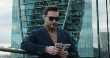 a successful businessman in a suit stands near a skyscraper and counts money. Successful business man counting money. american man checking bills, counting expences, examining credit balance