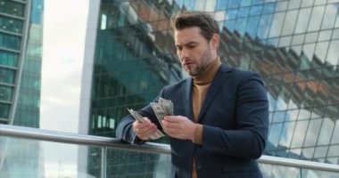 a successful businessman in a suit stands near a skyscraper and counts money. Successful business man counting money. american man checking bills, counting expences, examining credit balance