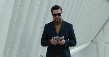 a successful businessman in a suit stands near a skyscraper and counts money. Successful business man counting money. american man checking bills, counting expences, examining credit balance