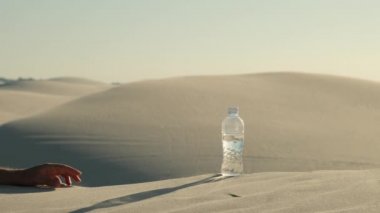 bottle with water on the desert. a plastic water bottle lies on the hot sand in the desert under the hot sun, alone in the middle of the desert sand. Hand takes a plastic water bottle in the desert.