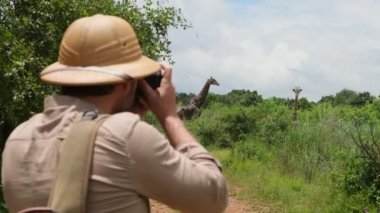 a male traveler takes a photo on a film camera of a giraffe in the savannah. giraffe in the savannah Serengeti National Park at sunset. Wild nature of Tanzania - Africa. Safari Travel Destination.