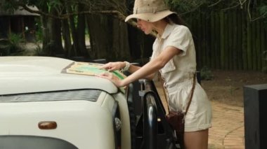 woman traveler with backpack looking to map. Holiday, journey, trip and summer summer travel concept. traveler stands near the safari car and looks at the route through the savannah on a paper map