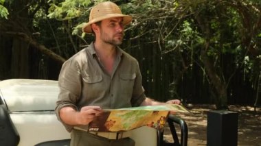 man traveler with backpack looking to map. Holiday, journey, trip and summer summer travel concept. traveler stands near the safari car and looks at the route through the savannah on a paper map