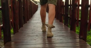 Hiker shoes on hiker legs standing above bridge. Hiker goes with trekking poles uphill. mens sports legs in trekking boots walk along a wooden bridge