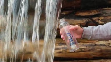 a man quenches his thirst on a hike in the forest from a mountain river. wave water surface with bubbles. a mans hand draws clean cold water from a mountain waterfall into a tourist bottle.