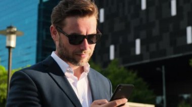 middle-aged man browsing internet reading news. man in glasses typing sms. Happy relaxed man holding his mobile phone. stylish man in a business suit and glasses uses a mobile phone on the street