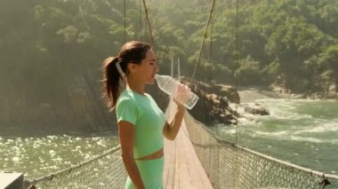 Güzel bir dişinin yakın çekimi okyanus kenarında güneşli bir akşamda koşudan sonra gider. Spor kıyafetleri giyen spor kızı sokakta, spor salonunda yoga yapıyor ve su içiyor.