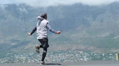 stylish man in sportswear jumping rope in the mountains. fitness, sport and exercising concept - man skipping with jump rope outdoors. Smiling american man in sportswear with fitness tracker jumping