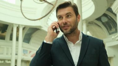 Yakışıklı genç iş adamı cep telefonuyla konuşuyor. Mutlu bir etnik erkek tasarımcının portresi ya da çekici görünümlü serbest çalışan, iş arkadaşıyla teması sürdürmek için cep telefonunu kullanıyor. Takım elbiseli bir adam.