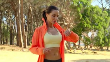 Cep telefonu ile çalışan kadın akıllı saate bağlandı. Arkasında dağ ağacı olan akıllı saat kullanan bir kadın. Fitness kadını ara veriyor, aktivite takip cihazını kontrol ediyor.
