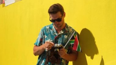 Güney Afrika bayrağını tutan erkek fotoğrafçı. Kasabada yürüyüşün keyfini çıkaran neşeli yaşlı erkek gezgin. Moda gözlüklü hippi adam tatilden memnun, gezmekten memnun, gülümseyen erkek gezgin