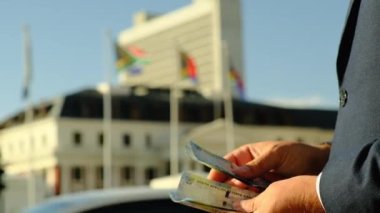 Adam Güney Afrika 'nın paralarını sayıyor. Güney Afrika bayrağının arka planında beyaz gömlek ve takım elbiseli Avrupalı bir işadamının ellerine yakın plan çekilmiş.