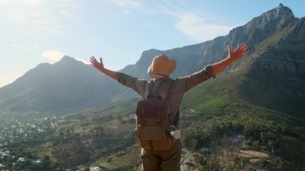 サファリウェアの男性旅行者が山の頂上にスポーツ用ハイキングシューズで登ってきます 男は日没の山でバックパックでハイキング旅行ライフスタイルさまよう冒険の概念 — ストック動画