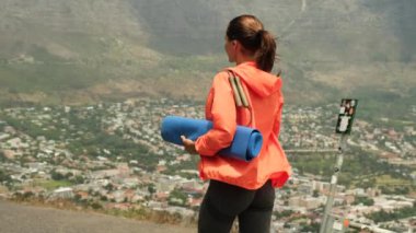 Fitness kadın koşucusu şehre koşmadan önce bacaklarını esnetiyor. Atletik kadın gün batımında dağlarda sıkı bir eğitimden sonra dinleniyor. Spor ceketli, bir şişe su ve yoga minderiyle atletik bir kız.