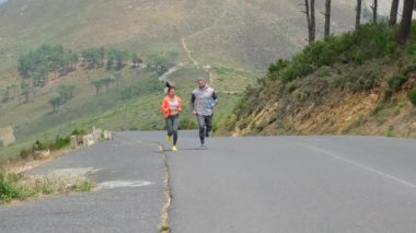 Spor çifti sabahın erken saatlerinde dağ yolunda koşuyor. Erkek ve kadın aşklarının portresi birlikte antrenman, spor ve sağlıklı konsept yapıyor. Aktif çift koşuyor