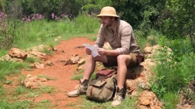 Sırt çantalı genç gezgin kayalıklarla dışarıda dinleniyor. Sırt çantası çekleriyle gezen genç bir gezgin vahşi doğada yön bulmak için haritayı çıkartıyor, gerçek bir kaşif. Seyahat Konsepti
