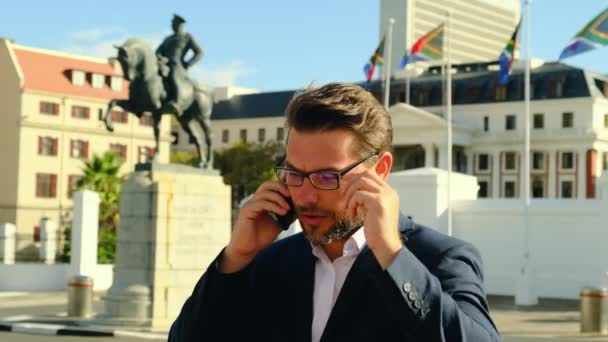 白い襟付きのビジネススーツの成功したヨーロッパの男は南アフリカの議会を背景に南アフリカのビジネス会社と電話で話します — ストック動画