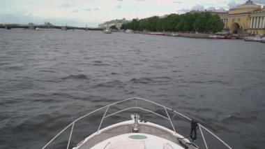 Lüks bir yat şehirde yelken açıyor. Yatın ön tarafında yay var. Beyaz gemi.