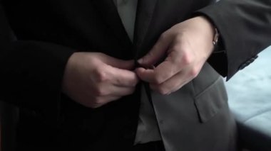 Adam siyah ceketin düğmesini bağlıyor. Erkek klasik bir takım elbise giyer..