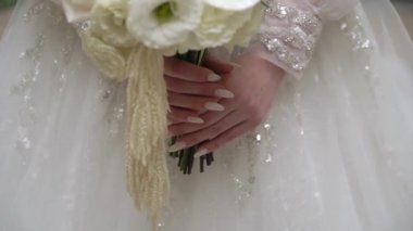 Gelinlik giymiş bir gelin elinde bir buket beyaz çiçek tutar..