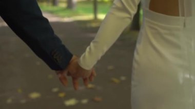 Gelin ve damat sonbahar parkında yürüyorlar. Düğün çifti el ele tutuşuyor..