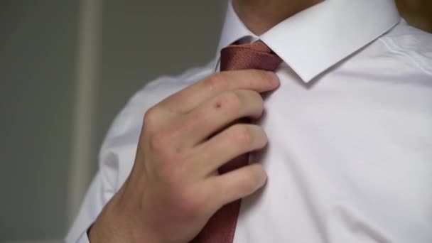 De man in het witte shirt trekt zijn bruine das recht. Jonge zakenman jurken voor werk — Stockvideo
