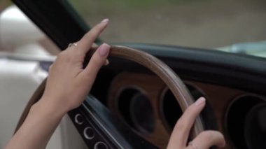 Genç kadın arabadaki tahta direksiyona dokunuyor. Kız sürücü.