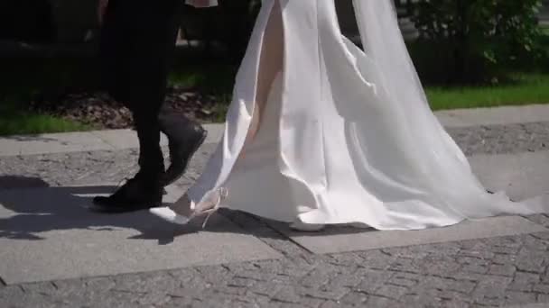 Menyasszony és vőlegény sétálnak a járdán. Férfiak és nők lába. — Stock videók