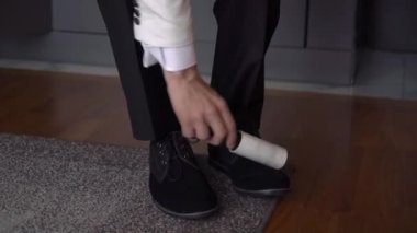 Klasik takım elbiseli bir adam giyinir, ayakkabılarını ve kıyafetlerini yapışkan bantla temizler..