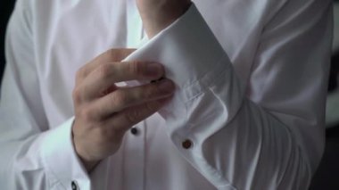 Adam kol düğmelerini takıyor. Beyaz gömlekli, kırmızı kravatlı ve mavi ceketli bir erkek..