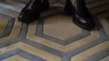 Takım elbiseli tanınmayan bir adam ve siyah klasik deri ayakkabılar halıda yürüyor.