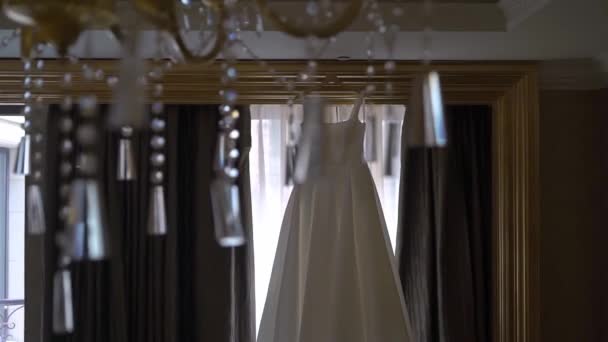 Svatební šaty visí na ramínku v ložnici u okna. Ráno nevěsty. — Stock video