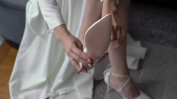 Наречена носить біле весільне взуття з підборами. Дівчинка у весільній сукні одягається.. — стокове відео