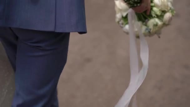 身穿蓝色西服的新郎带着一束玫瑰花和牡丹散步. — 图库视频影像