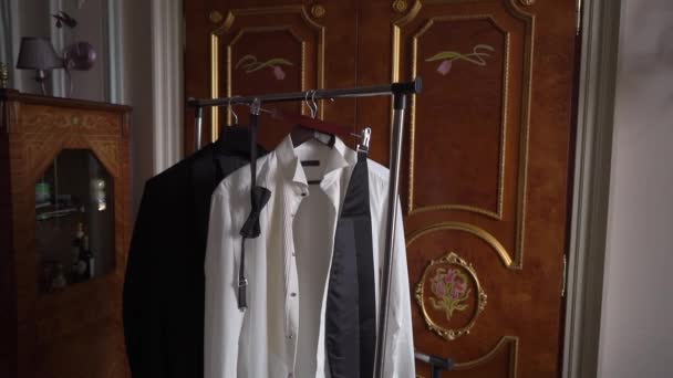 Male suit on a hanger in the bedroom. White shirt, black tuxedo jacket, bow tie. — Stockvideo