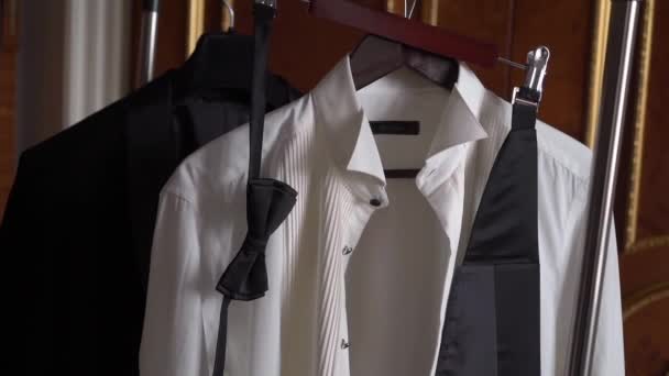 Male suit on a hanger in the bedroom. White shirt, black tuxedo jacket, bow tie. — Stockvideo
