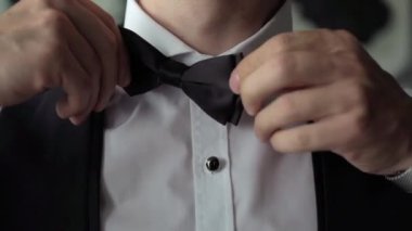Man in white shirt straightens his black bow tie. Young businessman dresses